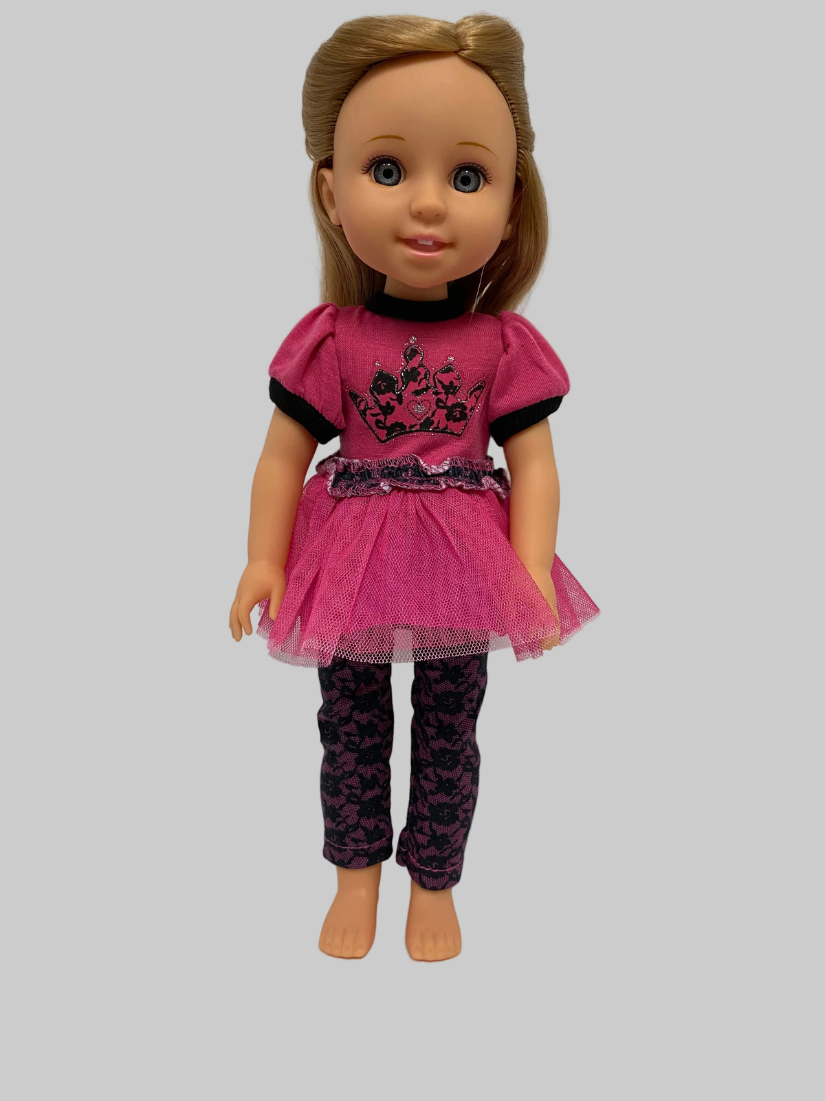 A doll with blonde hair wearing a pink and black dress with patterned tights, shown against a plain gray background.